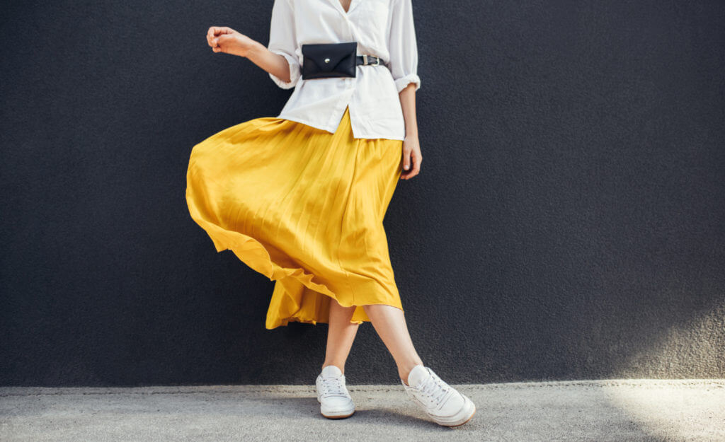 A closeup of a bright yellow skirt worn by a woman in white shoes and a white shirt.
